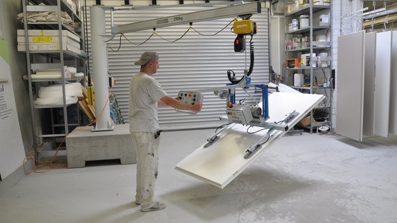 A wooden panel is lifted, turned and moved by means of a vacuum lifter