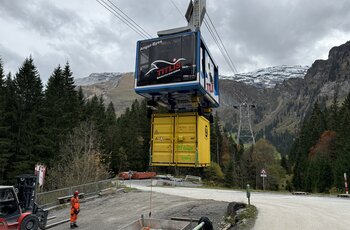 Système de transport de charges GIS A la station aval, la cabine prend en charge un conteneur pour le transport sous charge suspendue. L'opérateur commande le processus par radiocommande.