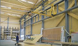 Dans un atelier de menuiserie, les planches de bois sont transportées à l'aide d'un système de grue.